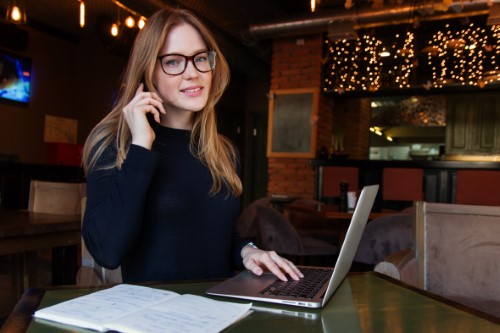 eight effective IVR characteristics woman working in cafe with phone and laptop